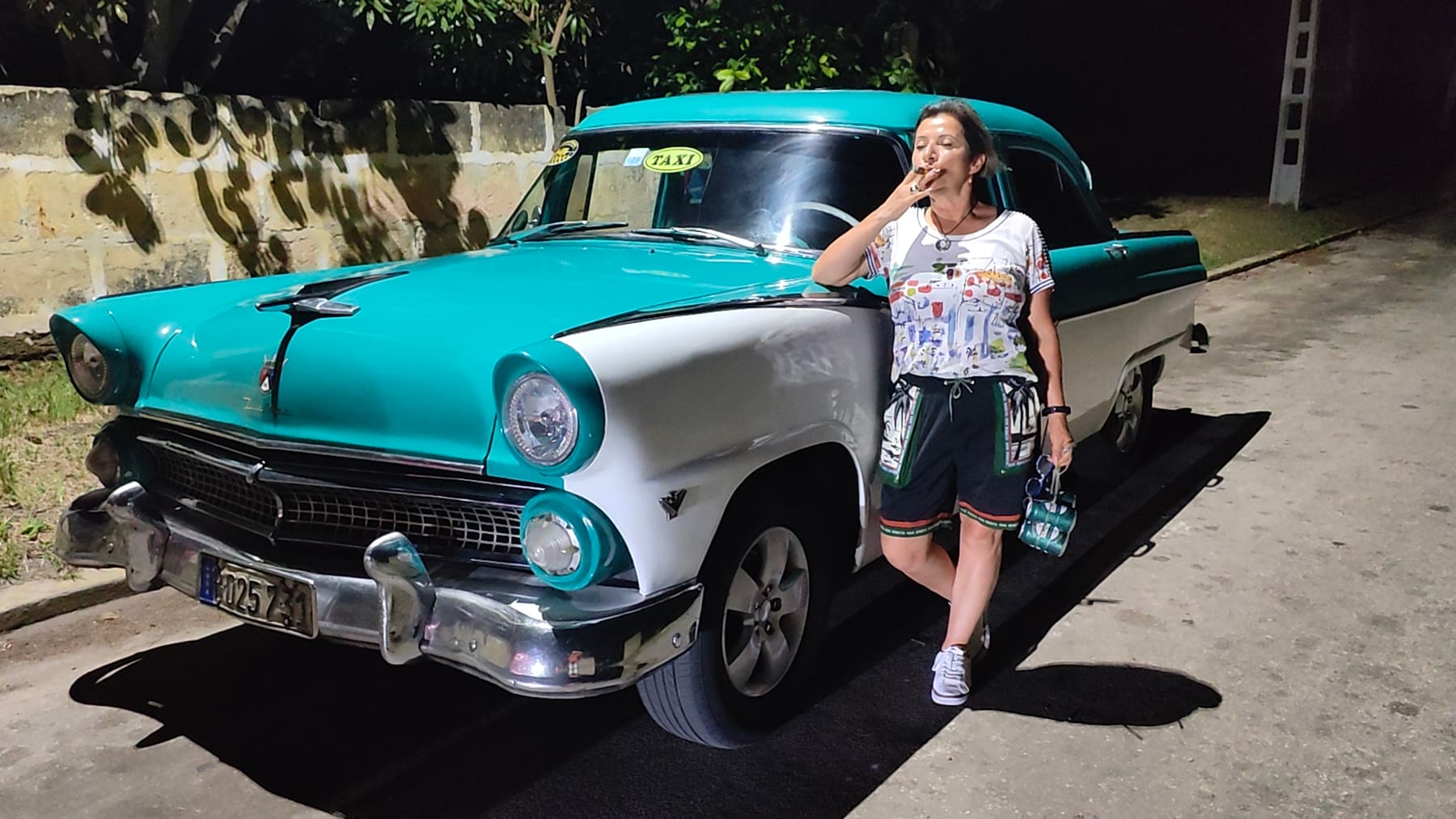 Beatriz junto a un carro antiguo turquesa en La Habana, de noche