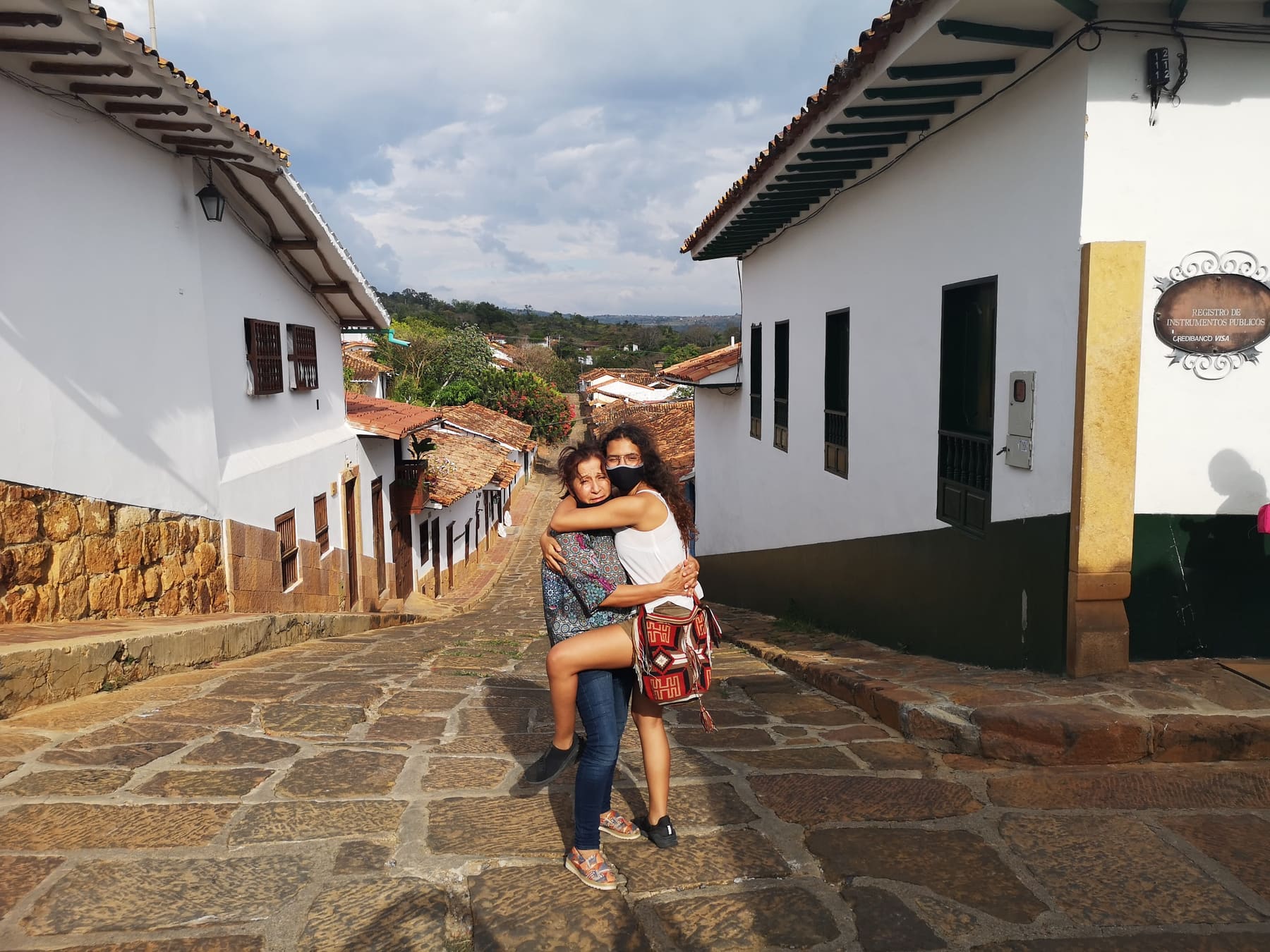 Beatriz abrazando a su hija en una calle de pueblo colonial